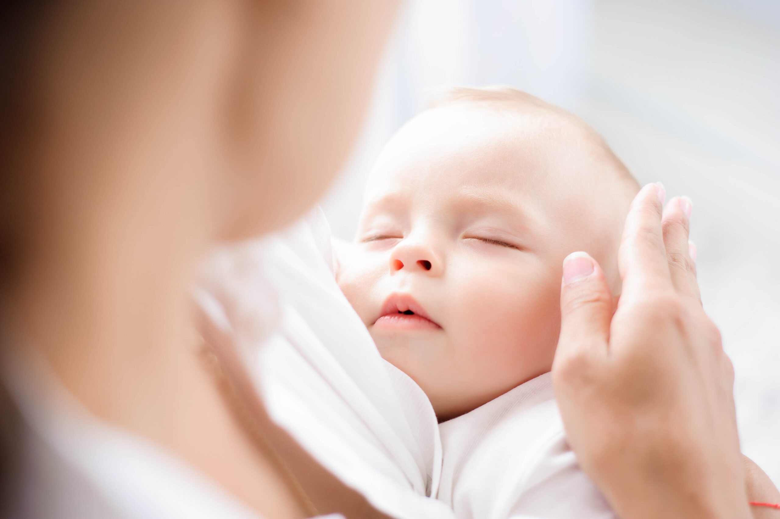 Baby sleeping on the mother’s chest. Young mother cuddling baby